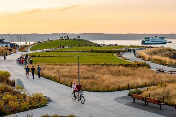 Pedestrians and bicyclists on wide paths surrounded by mown areas and prairie grasses with waterway in background.