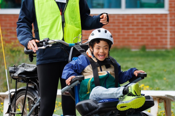 A young participant shows excitement for the bike ride; he is accompanied by a program staff wearing a neon vest.