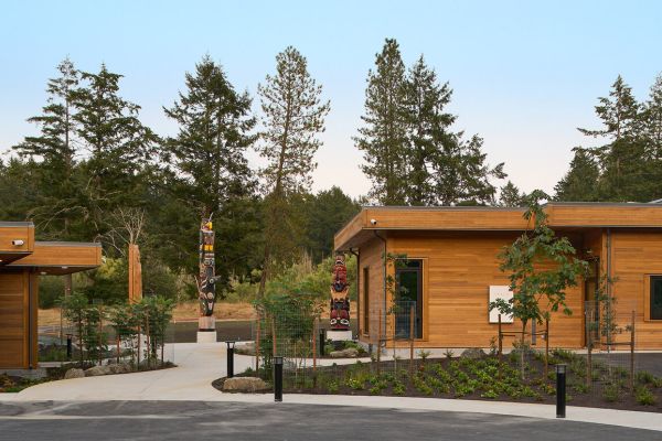 A sidewalk, path, and landscaped garden beds with flat-roofed, wood-sided buildings on either side.