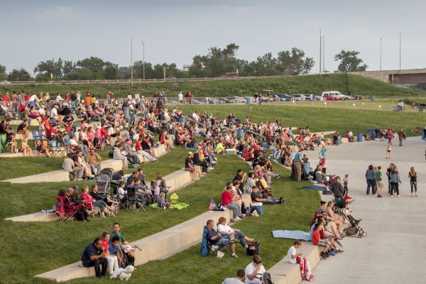 People sitting on stepped concrete seating in a gently sloping grassy hillside.