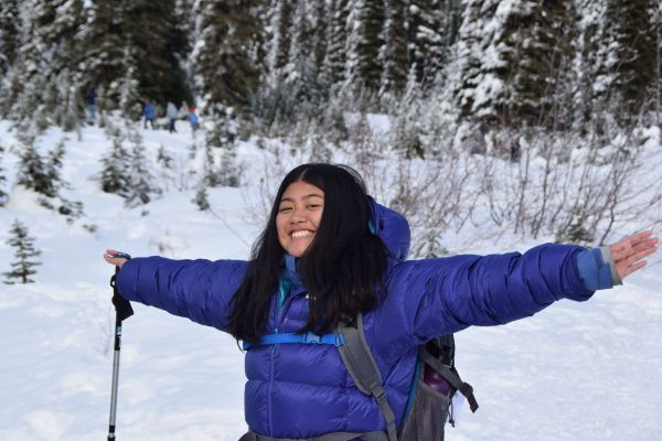 A participant poses with her arms stretched out, with snowy terrain as the background. Far behind her are other participants having fun in the snow.
