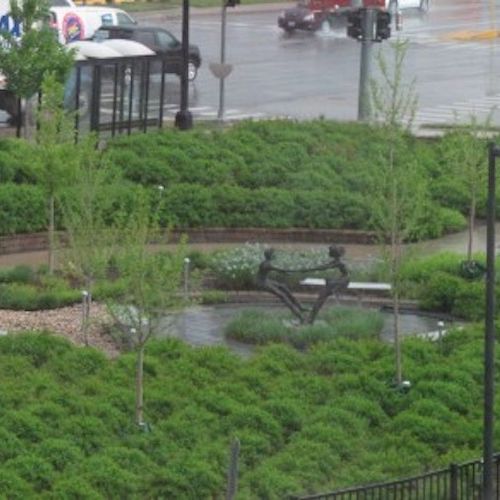 A bird’s-eye view of a spiral-shaped garden filled with plants, with a sculpture of children playing in the center. 
