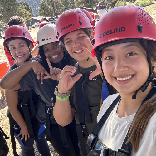 Four participants wearing safety helmets show confident smiles in their selfie.