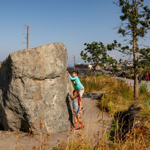 Children play on concrete forms resembling boulders while adults walk on wide paths.