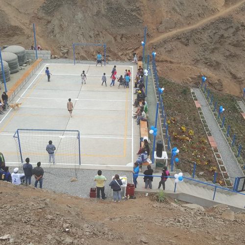 Photo shows a constructed area in a rocky hillside that features 6 cisterns, a court where people watch children playing soccer, and 3 rectangular terraced planting areas. The surrounding area appears to be arid as there is little natural vegetation.