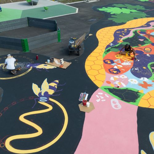 Artists painting the specialized ecological features along the literacy loop on the playground. They are painting a beehive design that features bees and other pollinators. 