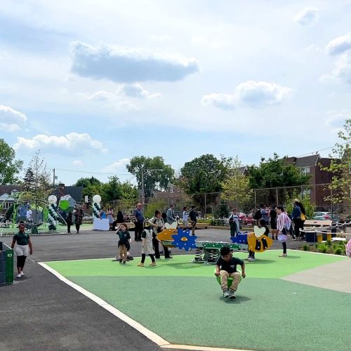 Under a bright sky students are climbing, spinning, walking, and gathering throughout the playground. 