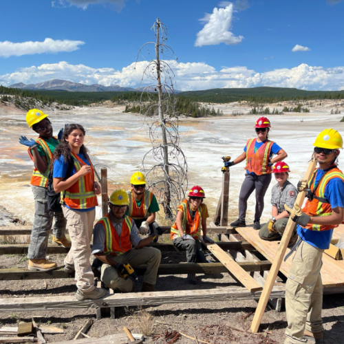 Groundwork youth equipped with orange vests and construction gear repair a boardwalk in Yellowstone National Park.