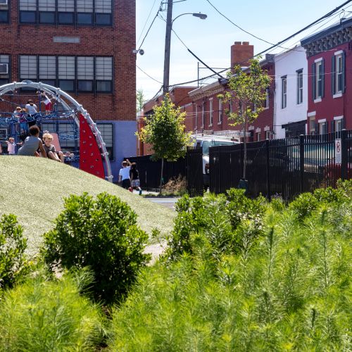 Children play on the climber dome. In the foreground are gardens filled with perennial plants and shrubs.