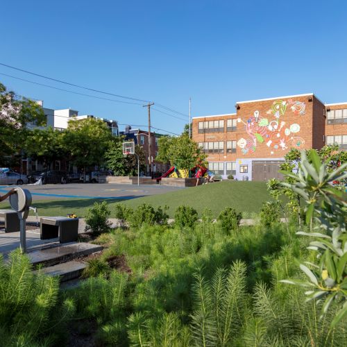 A child plays at the entrance to a sunken garden that is filled with vegetation. A building in the background is painted with colorful and playful artwork.