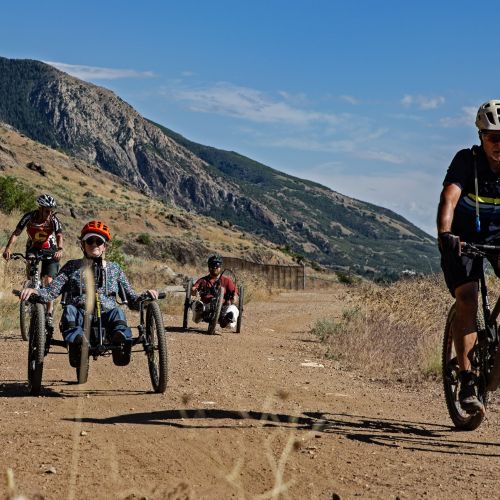 A group of participants learn mountain biking skills as they follow a trail together. There are different bikes to accommodate various needs.