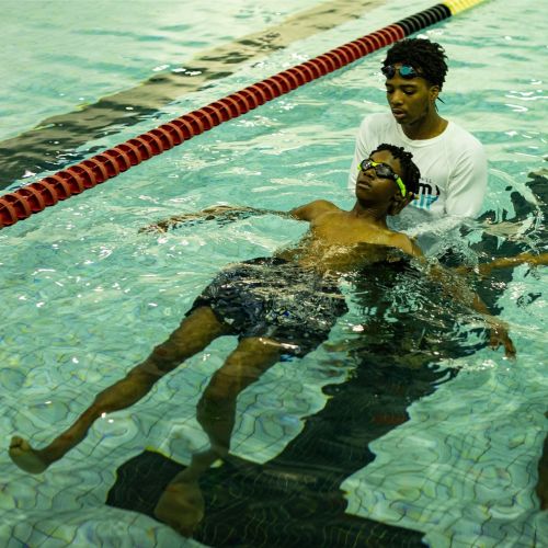A Making Waves participant is leaning back in the water while being supported by another individual