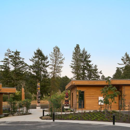 A sidewalk, path, and landscaped garden beds with flat-roofed, wood-sided buildings on either side.