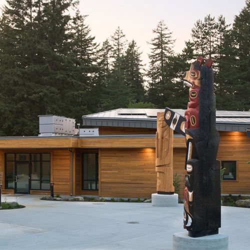 Three totem poles with a building and trees behind them.