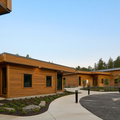 There’s a curved sidewalk and landscaped beds in front of and between wood-sided buildings.