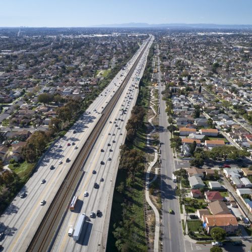 Aerial view shows an elevated freeway with a winding path on the right, and neighborhoods on either side.