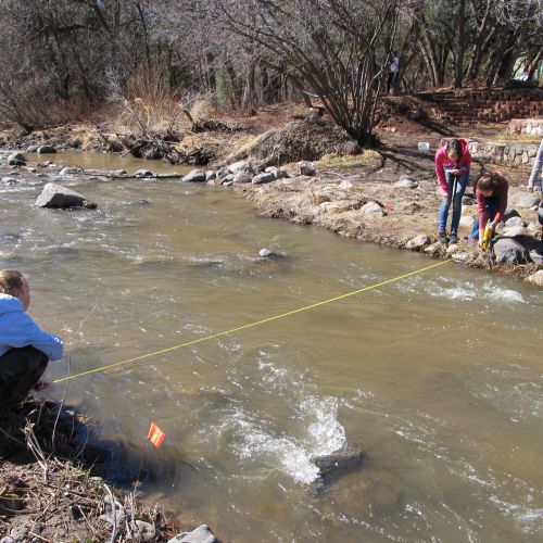 Students stand on each side of a coursing river measuring the width.