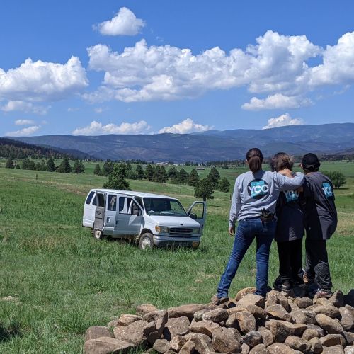 In preparation for soil conservation and erosion control, three interns gather closely and view the sprawling green landscape in front of them.