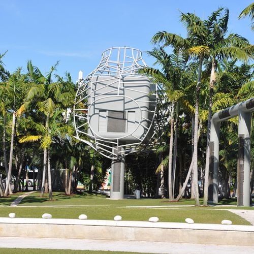 A tall mechanical structure in the center that houses the projector and outdoor sound system is flanked by palm trees, with a sidewalk in the foreground.