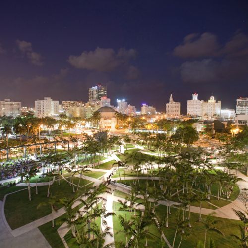 Nighttime aerial view of the illuminated park with the city skyline in the background.