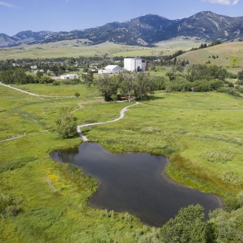 Aerial photo shows a body of water surrounded by areas of tall grass with buildings and mountains in the background.