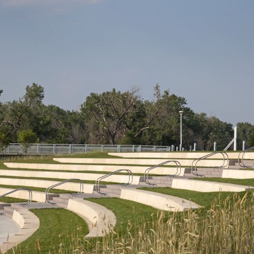 Series of stepped, concrete, bench-like seats are built into a gently sloping grassy hillside.