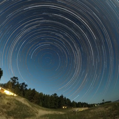 The image shows a timelapse of the night sky, with stars shining in a spiraling pattern.
