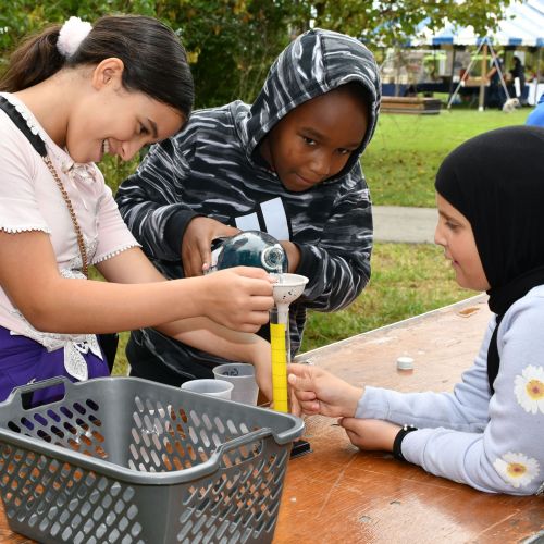Three students work at a table outside diligently testing the water quality of their local waterway using provided materials.