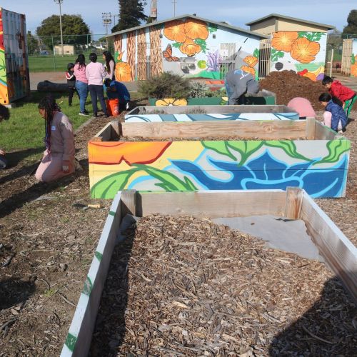 The wood that frames each garden bed and buildings at Nicholl Park boasts colorful, hand-painted murals. Youth work throughout the unplanted garden space.