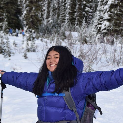  A participant poses with her arms stretched out, with snowy terrain as the background. Far behind her are other participants having fun in the snow.