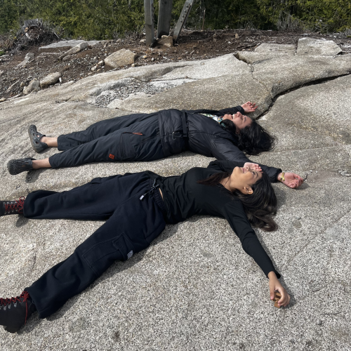 Two participants bask in the cool air as they lay sprawled on the flat face of a boulder, both wearing satisfied grins.